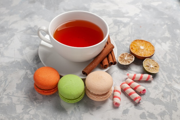 Vista frontal de una taza de té con macarons franceses en el escritorio de luz blanca