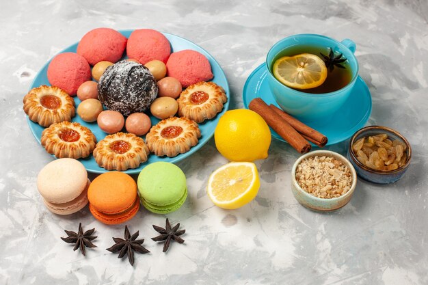 Vista frontal de una taza de té con macarons franceses, galletas y pasteles en la superficie blanca, galleta de galleta, pastel dulce, galleta de caramelo