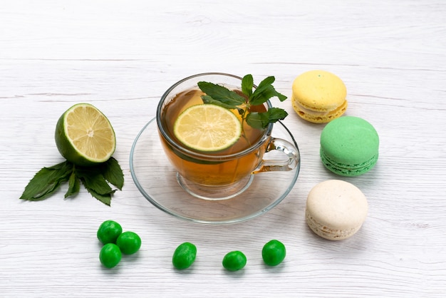 Vista frontal de una taza de té con macarons franceses y limón sobre blanco, galleta de pastel de té