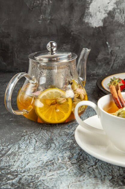 Vista frontal de una taza de té con panqueques y frutas en un desayuno matutino de superficie oscura