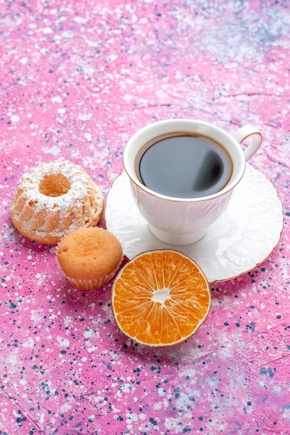 Vista frontal de la taza de té con pastelito sobre superficie rosa