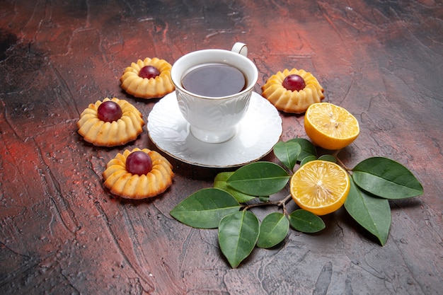 Vista frontal de una taza de té con pequeñas galletas sobre fondo oscuro