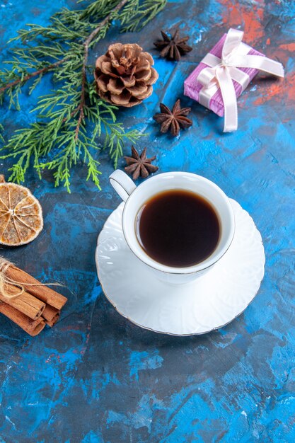 Vista frontal de una taza de té platillo blanco ramas de pino ramas de canela anís estrellado rodajas de limón seco sobre fondo azul.