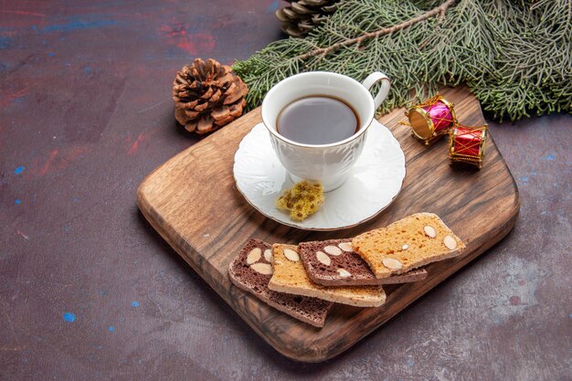 Vista frontal de una taza de té con rebanadas de pastel en el espacio oscuro