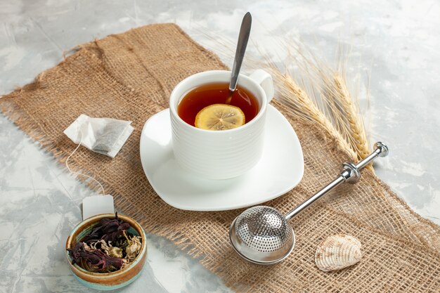 Vista frontal de una taza de té con una rodaja de limón sobre la superficie blanca