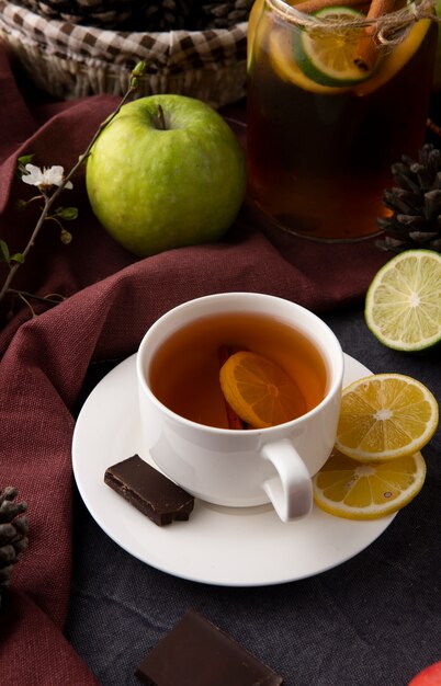 Vista frontal taza de té con rodajas de limón y chocolate negro con una manzana verde sobre la mesa