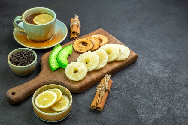 Vista frontal de una taza de té con rodajas de limón y frutos secos sobre una superficie oscura