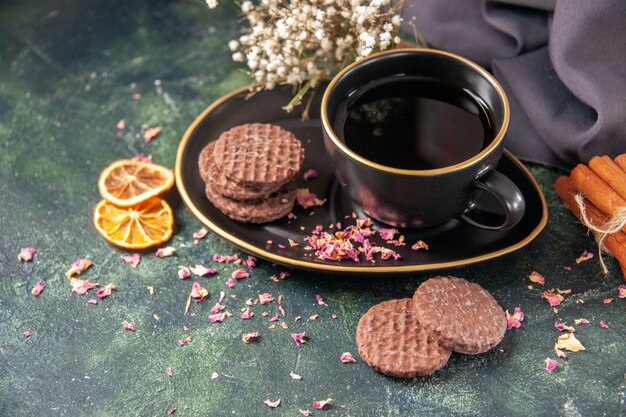 Vista frontal de una taza de té en una taza negra y un plato con galletas sobre una superficie azul oscuro, color azul oscuro, azúcar, vidrio, desayuno, postre, pastel, ceremonia de la galleta