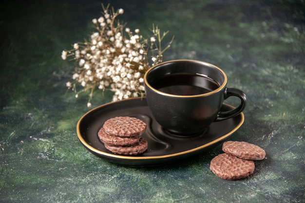 Vista frontal de la taza de té en la taza y el plato negro con galletas en la superficie oscura de color azúcar de cristal de postre ceremonia de galletas