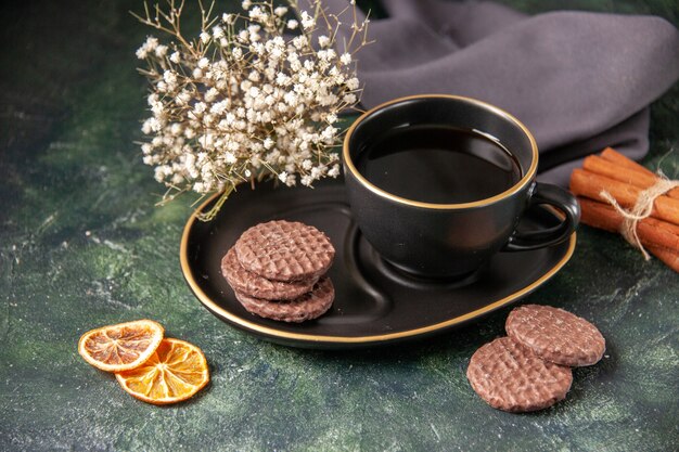 Vista frontal de la taza de té en la taza y el plato negro con galletas en la superficie oscura de color azúcar de vidrio desayuno postre pastel galletas ceremonia
