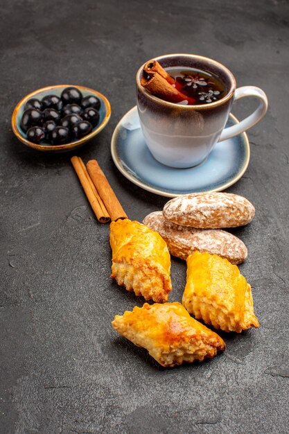 Vista frontal de la taza de té con tortas en galletas de pastel de pastelería de superficie oscura