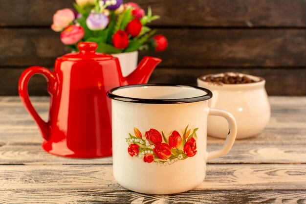 Vista frontal de la taza vacía con caldera roja café marrón semillas y flores en el escritorio de madera