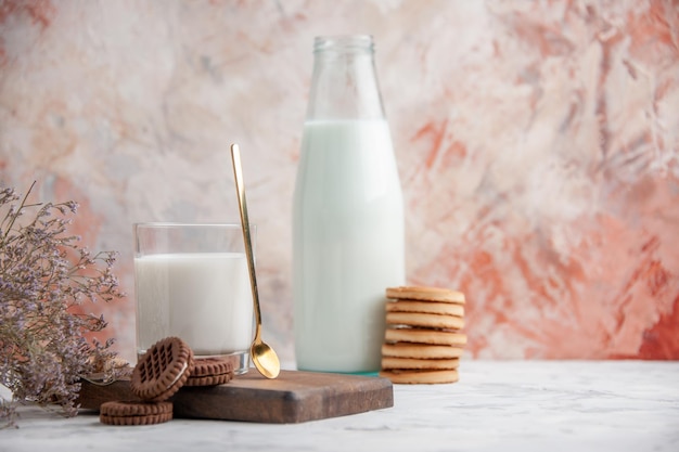 Vista frontal de la taza de vidrio y en botella llena de galletas de leche en la flor de tablero de madera sobre fondo de hielo