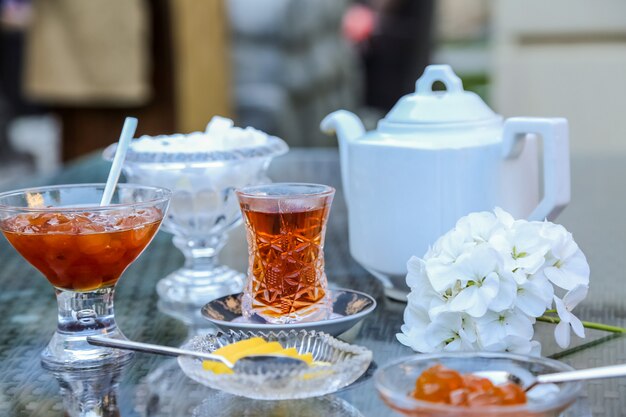 Vista frontal de té en vidrio armudu con mermelada de cereza blanca y rodajas de limón sobre la mesa