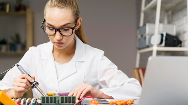 Vista frontal del técnico femenino con placa electrónica y soldador