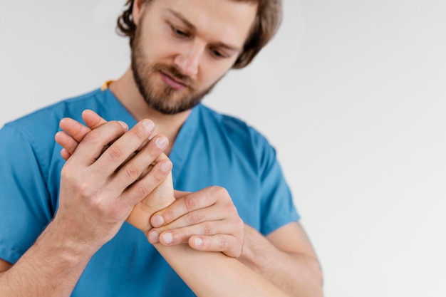 Vista frontal del terapeuta osteopático masculino comprobando la articulación de la muñeca del paciente femenino