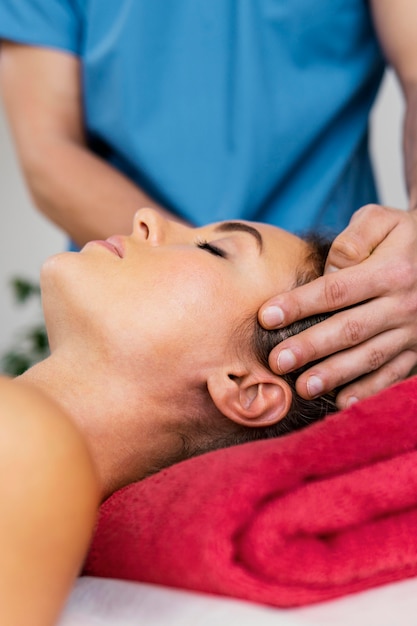 Vista frontal del terapeuta osteopático masculino comprobando la columna del cuello del paciente femenino