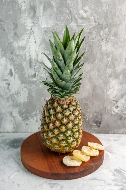 Vista frontal de toda la piña dorada fresca y limas en la tabla de cortar de pie sobre la superficie de mármol