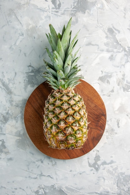 Vista frontal de toda la piña dorada fresca en la tabla de cortar sobre la superficie de mármol