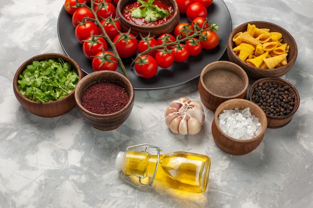 Vista frontal de los tomates cherry frescos dentro de la placa con verduras y diferentes condimentos en la superficie blanca ensalada de salud alimentaria comida vegetal