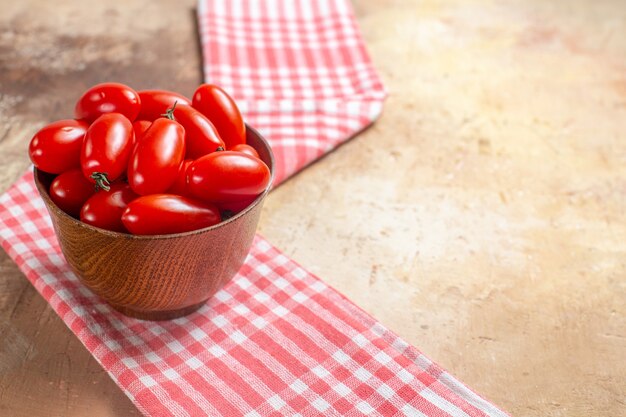 Vista frontal de los tomates cherry en un tazón de madera una toalla de cocina sobre fondo ámbar espacio libre