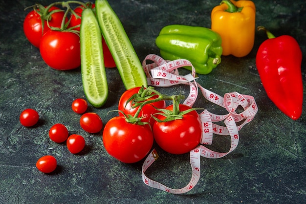 Vista frontal de tomates frescos, pimientos y pepinos medidores en la superficie de colores oscuros con espacio libre