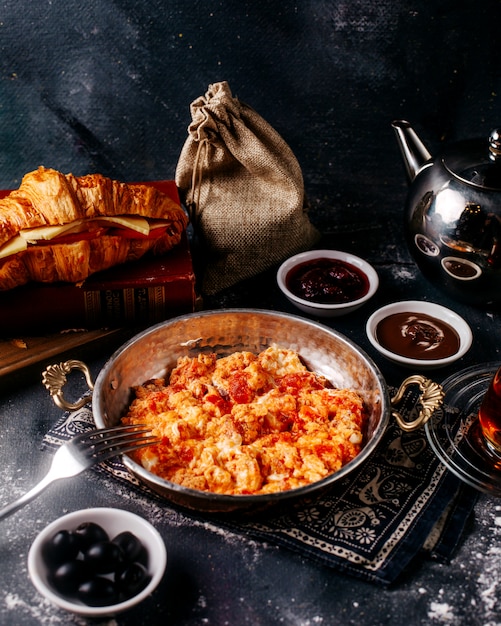 Vista frontal tomates fritos huevos sabrosos junto con aceitunas pan y té en el piso gris