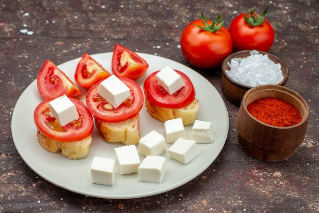 Vista frontal de tomates y queso dentro de un plato blanco con condimentos en marrón