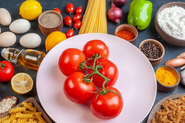 Vista frontal de tomates rojos con condimentos de verduras de pasta cruda y en la oscuridad