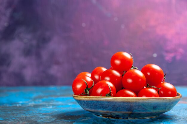 Vista frontal de los tomates rojos frescos dentro de la placa sobre el cuadro azul