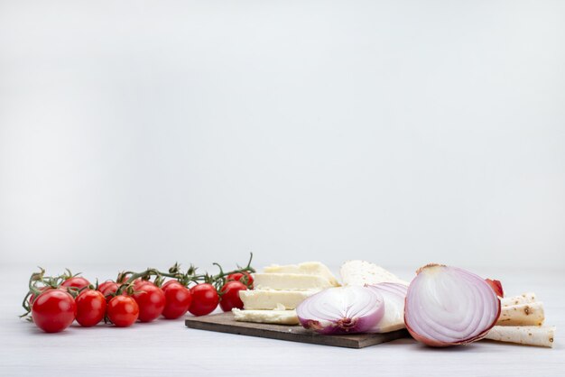 Vista frontal de tomates rojos frescos junto con queso blanco y cebollas en blanco