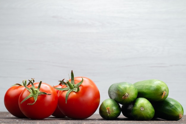 Vista frontal tomates rojos frescos maduros junto con pepinos verdes en blanco, comida de comida vegetal