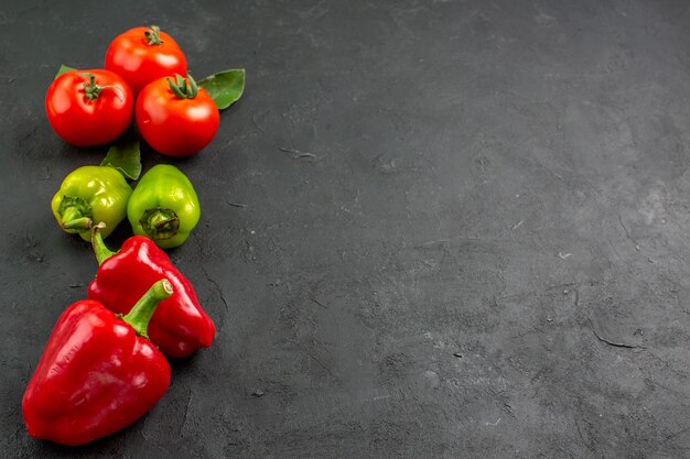 Vista frontal de tomates rojos frescos con pimientos sobre fondo oscuro