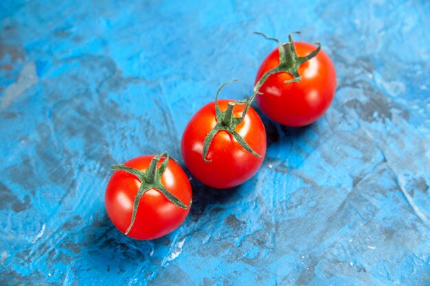 Vista frontal de tomates rojos frescos sobre la mesa azul