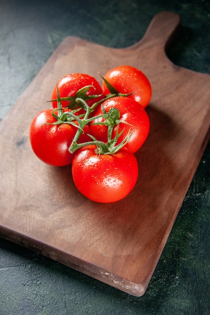 Vista frontal de tomates rojos frescos en la tabla de cortar fondo oscuro