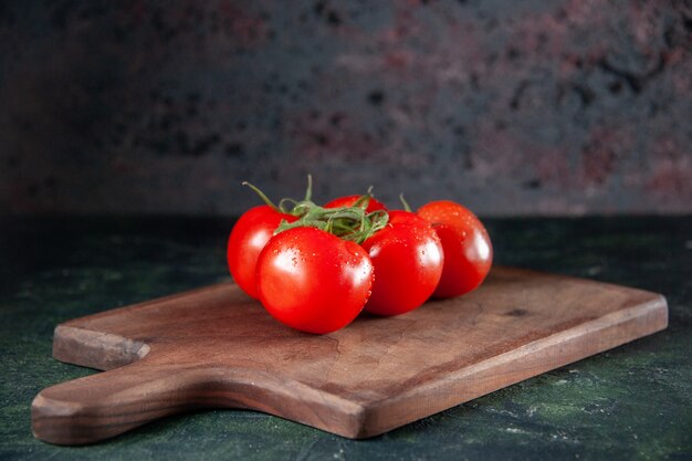 Vista frontal de tomates rojos frescos en la tabla de cortar fondo oscuro