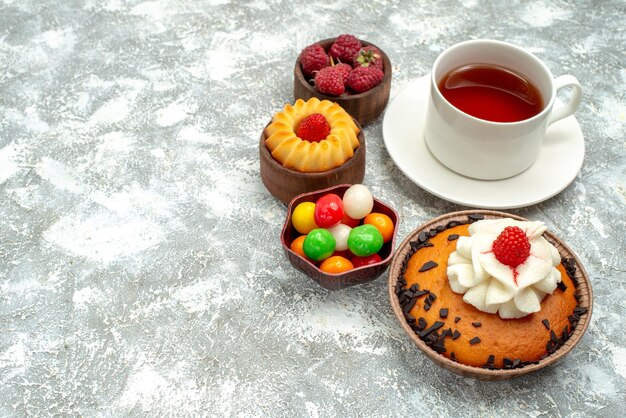 Vista frontal de la torta de chispas de chocolate con una taza de té y caramelos sobre fondo blanco pastel dulce galleta bizcocho de azúcar