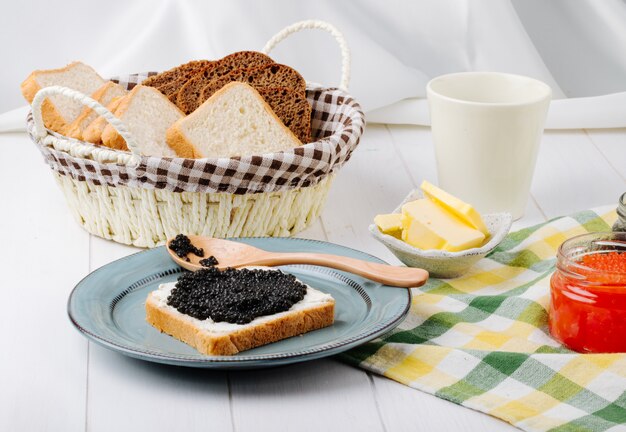 Vista frontal tostadas con caviar negro con una cuchara en un plato con mantequilla de caviar rojo y pan en una cesta