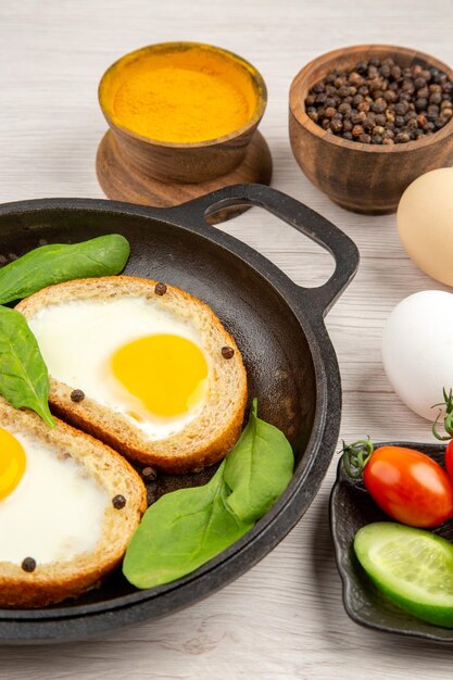 Vista frontal tostadas de huevo con condimentos y pepinos en rodajas sobre un fondo blanco comida color desayuno almuerzo plato pan té comida