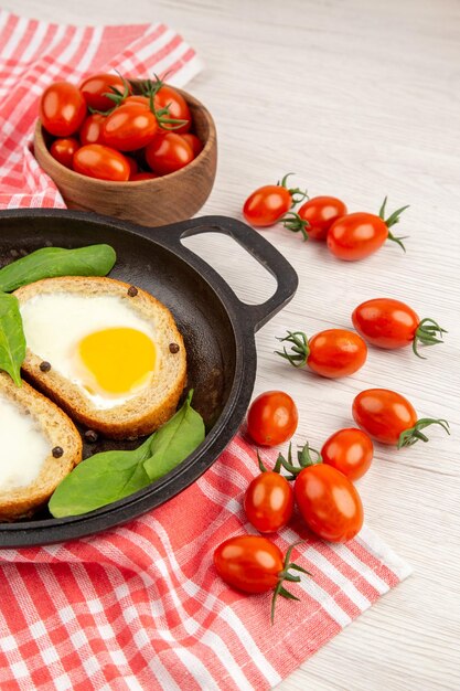 Vista frontal tostadas de huevo dentro de la sartén con tomates rojos sobre fondo blanco almuerzo comida té comida pan color desayuno