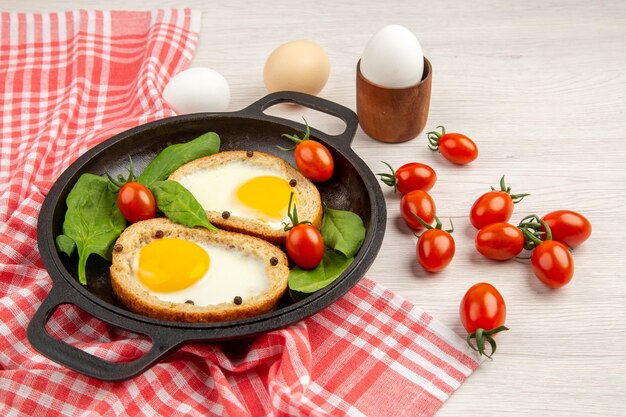 Vista frontal tostadas de huevo dentro de la sartén con tomates sobre fondo blanco pan color almuerzo plato desayuno comida té comida