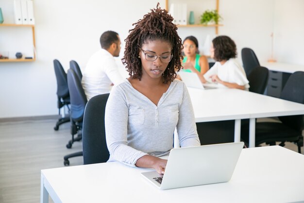 Vista frontal del trabajador atractivo enfocado escribiendo en la computadora portátil