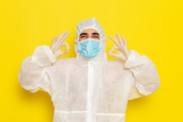 Vista frontal del trabajador científico masculino en traje blanco de protección especial con máscara en el escritorio amarillo trabajador científico química científica peligro de color