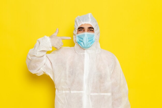 Vista frontal del trabajador científico masculino en traje blanco de protección especial con máscara en la pared amarilla