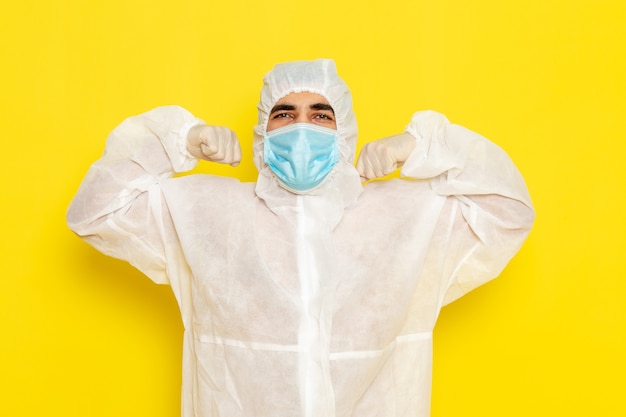 Foto gratuita vista frontal del trabajador científico masculino en traje blanco protector especial con máscara flexionando sobre pared amarilla
