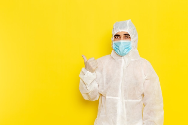 Vista frontal del trabajador científico masculino en traje blanco protector especial con máscara en la pared de color amarillo claro
