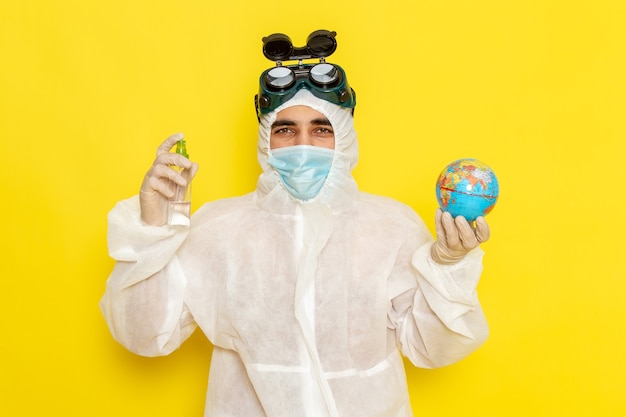 Foto gratuita vista frontal trabajador científico masculino en traje especial sosteniendo un pequeño globo redondo y rociar sobre una superficie amarilla