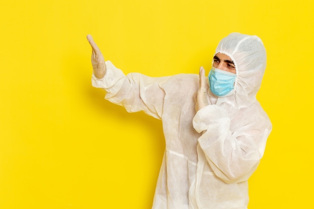 Vista frontal del trabajador científico masculino en traje de protección especial y con máscara en la pared de color amarillo claro