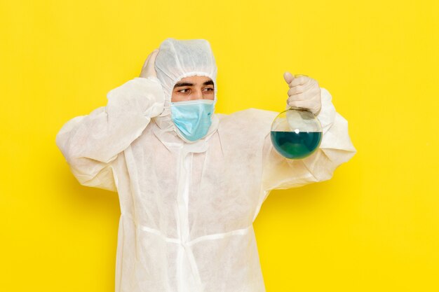 Foto gratuita vista frontal del trabajador científico masculino en traje de protección especial con máscara que sostiene el matraz en la pared de color amarillo claro