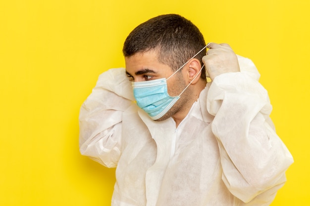 Vista frontal del trabajador científico masculino en traje de protección especial con su máscara en el escritorio amarillo traje de trabajador científico peligro de color